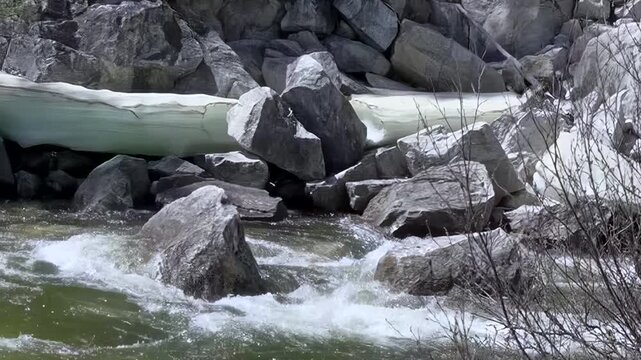 Crystal clear water rushes dynamically over ancient rocks near Lake Khuvsgul, Mongolia. Patches of luminous ice cling to the banks, revealing the powerful melt of a pristine spring day in the wild.