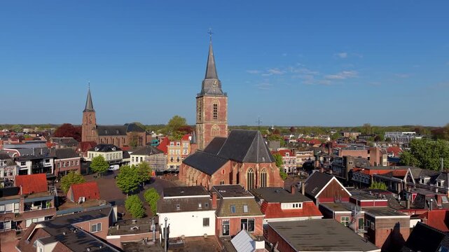 An aerial drone view of a historic European town center featuring two large brick churches with tall spires rising above a public market square surrounded by traditional houses and shops.
