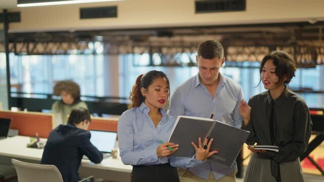 Three colleagues collaborate on business documents and charts in a contemporary office. Diverse employees engage in a productive discussion, reviewing important project data