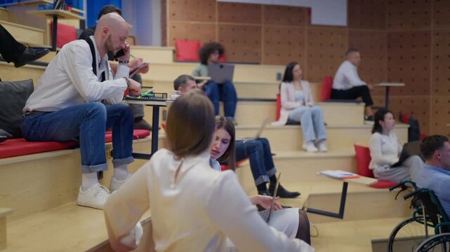 Diverse people engage in a collaborative work environment, some using laptops and others discussing. A group of colleagues gather in a contemporary amphitheater-style space, focused on their tasks