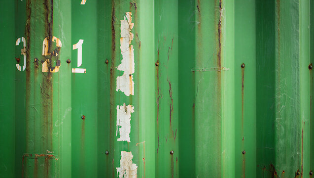 Green industrial shipping container wall texture showing faded paint and signs of oxidation and weathering with container corrugated shipping industrial background weathered oxidized