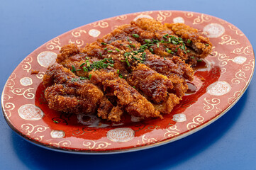 Fototapeta premium Chinese-style crispy fried pork coated with savory sauce, topped with sesame seeds and chopped chives, served on a decorative ceramic plate.