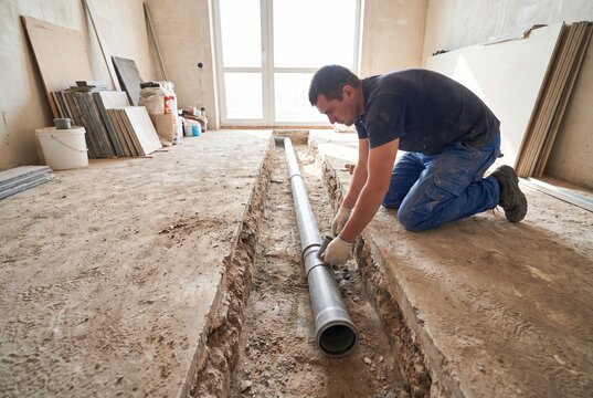 Construction worker installing a large diameter pipe in a trench on a building site with natural light.