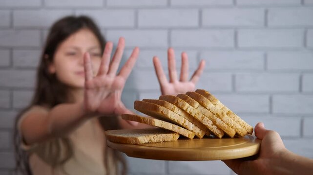 Gluten-free diet. Young girl refusing to eat bread with a stop hand gesture, illustrating the concept of a gluten-free diet, celiac disease, or an eating disorder due to carbohydrate intolerance