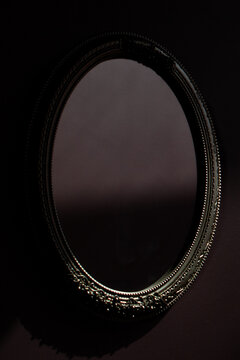 An ornate silver mirror reflecting a dark gothic wall