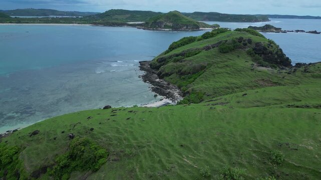 High Drone View Curved Turquoise Bay And Reef With Visible Coral Formations, Crescent White Beach, Emerald Hills And Shallow Lagoon Pools Bright Midday Light, Bukit Merese, Lombok, Tanjung Ann beach