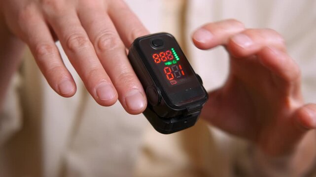 Person measuring blood oxygen saturation level with pulse oximeter. Close-up view of a person wearing a medical fingertip pulse oximeter and monitoring the digital display