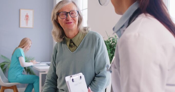 Caring and friendly doctor or nurse welcomes a senior female patient for a medical appointment in the clinic office, offering consultation, treatment and aid to support healthcare needs.