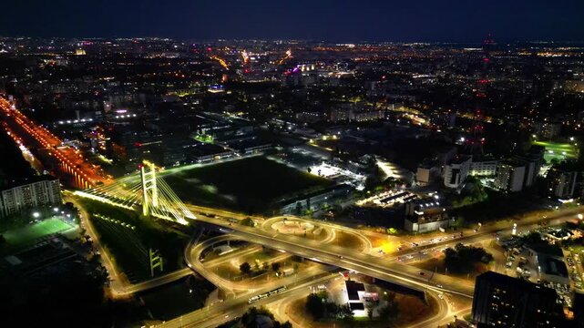 Cinematic high angle night view of the illuminated Ciurel bridge in Bucharest, Romania. Modern cable-stayed overpass surrounded by vibrant city traffic lights.