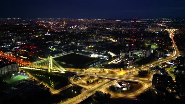 Cinematic high angle night view of the illuminated Ciurel bridge in Bucharest, Romania. Modern cable-stayed overpass surrounded by vibrant city traffic lights.