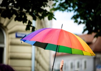 Colorful rainbow umbrella in urban setting with green foliage and classic architecture during pride parade in Klagenfurt Austria © HelgaQ