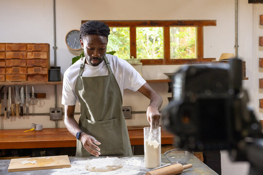Adult man wearing green apron handling dough in home bakery by camera, reaching flour jar