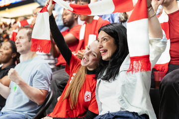 Fototapeta premium Cheerful women singing fans waving scarves and cheering for national team, stadium with excited crowd shouting. Exciting football match packed with rivalry and anticipation, fan emotion.