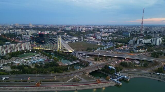 Cinematic high angle night view of the illuminated Ciurel bridge in Bucharest, Romania. Modern cable-stayed overpass surrounded by vibrant city traffic lights.