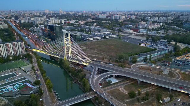 Cinematic high angle night view of the illuminated Ciurel bridge in Bucharest, Romania. Modern cable-stayed overpass surrounded by vibrant city traffic lights.