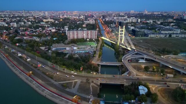 Cinematic high angle night view of the illuminated Ciurel bridge in Bucharest, Romania. Modern cable-stayed overpass surrounded by vibrant city traffic lights.
