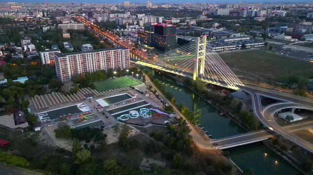 Cinematic high angle night view of the illuminated Ciurel bridge in Bucharest, Romania. Modern cable-stayed overpass surrounded by vibrant city traffic lights.