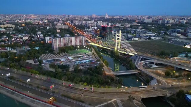 Cinematic high angle night view of the illuminated Ciurel bridge in Bucharest, Romania. Modern cable-stayed overpass surrounded by vibrant city traffic lights.