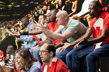 Obraz premium Red team football supporters showing mixed emotions in packed stadium stands during tense live soccer match, scarves, horns and crowd reactions. Upset fans in shock, football defeat frustration.