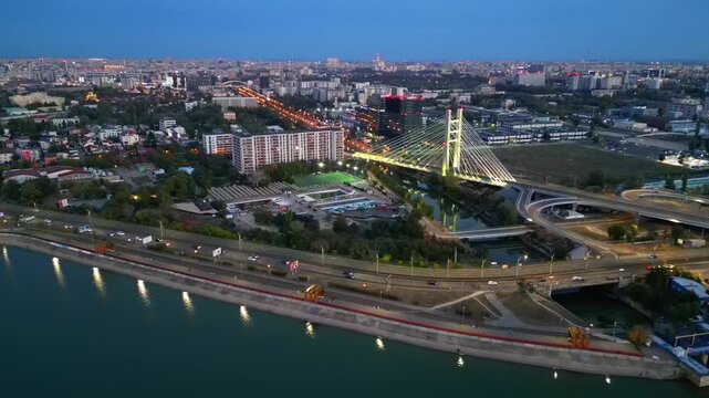Cinematic high angle night view of the illuminated Ciurel bridge in Bucharest, Romania. Modern cable-stayed overpass surrounded by vibrant city traffic lights.