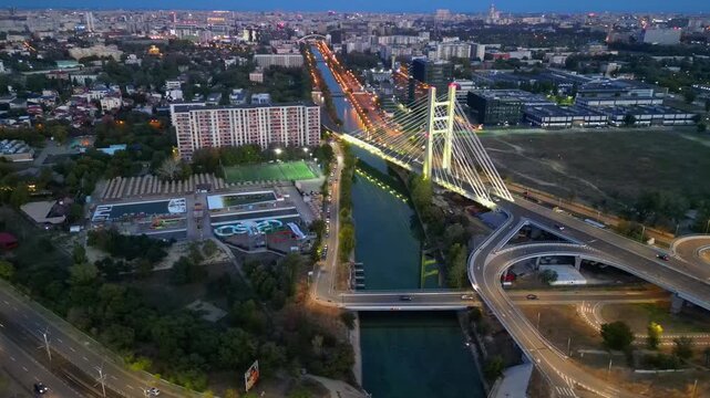 Cinematic high angle night view of the illuminated Ciurel bridge in Bucharest, Romania. Modern cable-stayed overpass surrounded by vibrant city traffic lights.