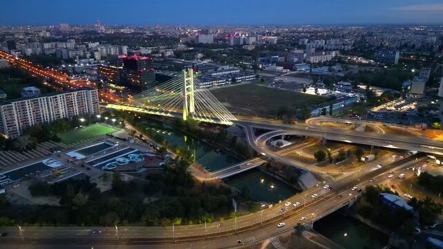 Cinematic high angle night view of the illuminated Ciurel bridge in Bucharest, Romania. Modern cable-stayed overpass surrounded by vibrant city traffic lights.