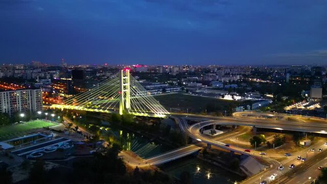 Cinematic high angle night view of the illuminated Ciurel bridge in Bucharest, Romania. Modern cable-stayed overpass surrounded by vibrant city traffic lights.
