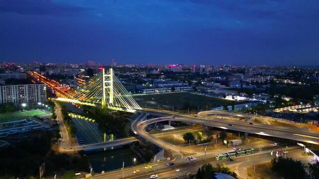 Cinematic high angle night view of the illuminated Ciurel bridge in Bucharest, Romania. Modern cable-stayed overpass surrounded by vibrant city traffic lights.