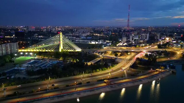 Cinematic high angle night view of the illuminated Ciurel bridge in Bucharest, Romania. Modern cable-stayed overpass surrounded by vibrant city traffic lights.