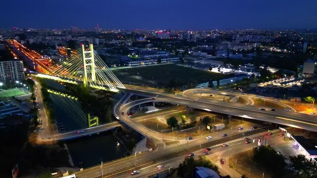 Cinematic high angle night view of the illuminated Ciurel bridge in Bucharest, Romania. Modern cable-stayed overpass surrounded by vibrant city traffic lights.
