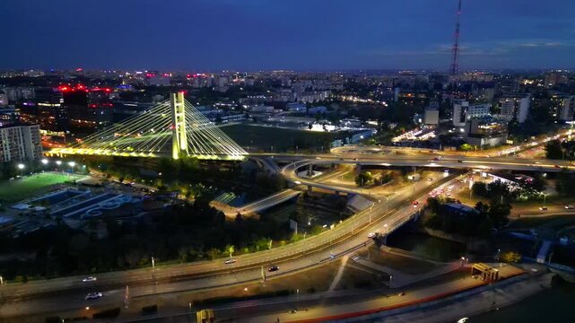 Cinematic high angle night view of the illuminated Ciurel bridge in Bucharest, Romania. Modern cable-stayed overpass surrounded by vibrant city traffic lights.