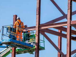 Naklejka premium Structural steel erection, building construction, involving the placement and bolting of large steel beams to create frameworks. Ironworkers use specialized equipment like aerial lifts and cranes. 