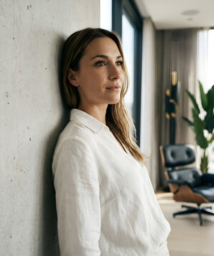 Serene portrait of a young woman leaning against a wall in a modern minimalist interior, soft natural light, calm atmosphere, lifestyle and interior conce