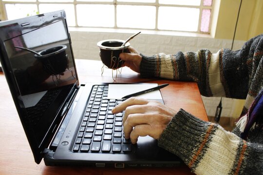 Hombre trabajando de forma remota desde su hogar utilizando una computadora port&aacute;til mientras toma mate. Refleja productividad, teletrabajo, comodidad, equilibrio entre la vida laboral y personal.