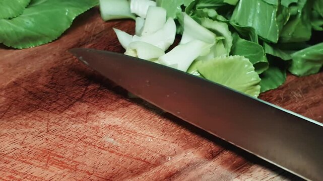 Chef knife and chopped bok choy on a rustic wooden cutting board.