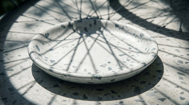 White terrazzo plate with bicycle wheel shadow on matching table