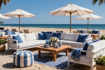 Obraz premium White outdoor sofas and chairs with blue cushions sit on sand by the ocean. Beach umbrellas provide shade over wood tables with vases and cups. A peaceful seaside lounge.