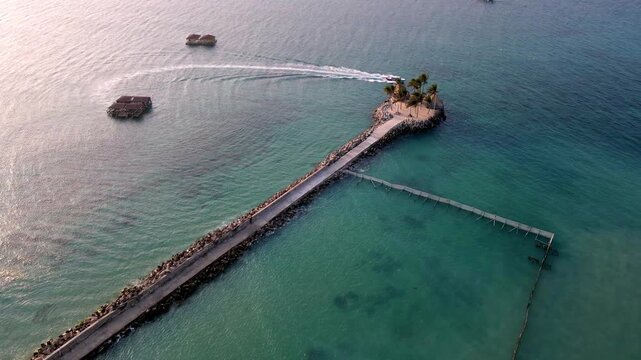 Aerial view of palm islet and causeway in turquoise sea with speedboat