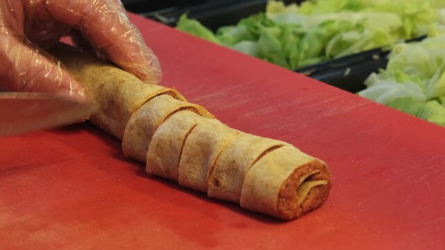 Close up video of a Turkish chef slicing a spicy cig kofte roll with a sharp knife on the counter, creating a unique sushi style fusion presentation with expert culinary skills