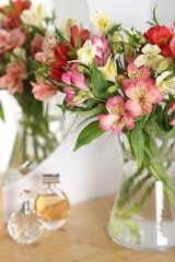 Obraz premium Bouquet of alstroemeria flowers in vase and perfumes on dressing table indoors, closeup