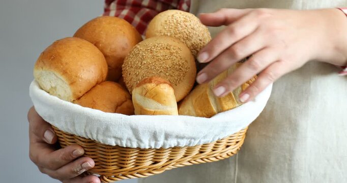 Woman holding wicker basket with different types of bread indoors, closeup