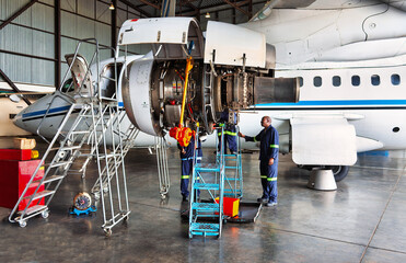 Two plane technicians working on open turboprop airplane engine during mechanical inspection and repair inside hangar. © poco_bw