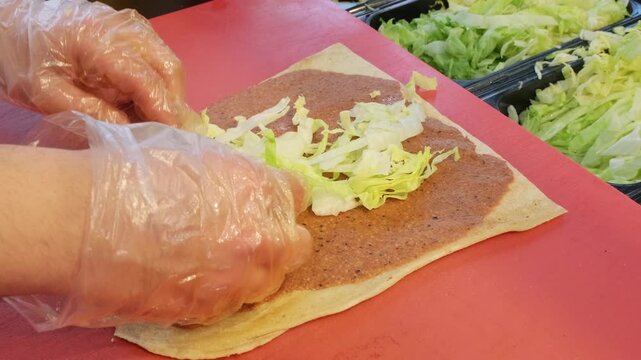 A detailed close up video of a master chef adding fresh lettuce and sliced tomatoes over spicy cig kofte on lavash bread, preparing a traditional authentic Turkish wrap.
