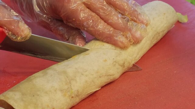 A close up video of a master chef expertly slicing a freshly prepared traditional spicy cig kofte wrap diagonally with a sharp knife on the counter, showcasing Turkish street food preparation.