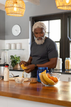 Senior African American man peeling banana at wooden kitchen counter, using blender base