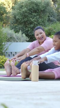 Vertical video: Stretching mom and daughter reaching toes on patio mats with watch bottle in pink