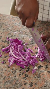 Vertical video: Gripping blue knife, cook hands cutting red cabbage on speckled counter for slaw