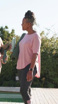 Vertical video: Chatting, woman holding mat  and  bottle in pink at pool gesturing preparing for yog