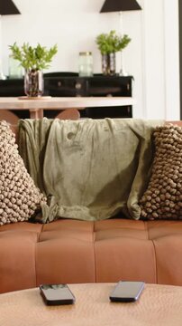 Vertical video: Shifting camera revealing brown sofa with olive throw at home showing two phones
