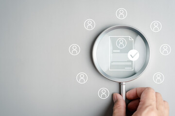 Human resource management and recruitment concept for business hiring. Hand holding magnifying glass focusing on resume with checkmark.